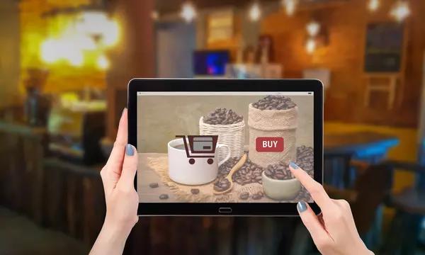 A person holds a tablet showing an online store for coffee, with coffee beans and a cup. 