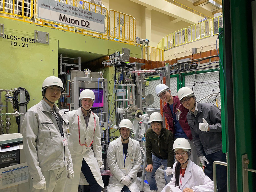 七名研究人员戴着白色安全帽，身穿实验服，在大型实验设备前合影留念。上面的标牌上写着：Muon D2。