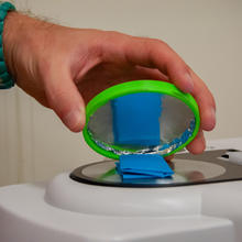 A close-up shot of hand holding a circular lid over a piece of blue clothing on top of a scientific device.