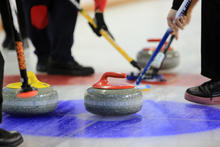 photo of four people holding pucks pushing curling stones