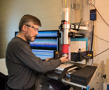 Scientist puts material down below a tube. Background: computer screen