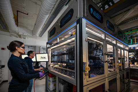 NIST研究人员伊丽莎白·斯特里查尔斯基（Elizabeth Strychalski）和大卫·罗斯（David Ross）为NIST生物铸造厂的箱形结构中的机器人手臂编程。