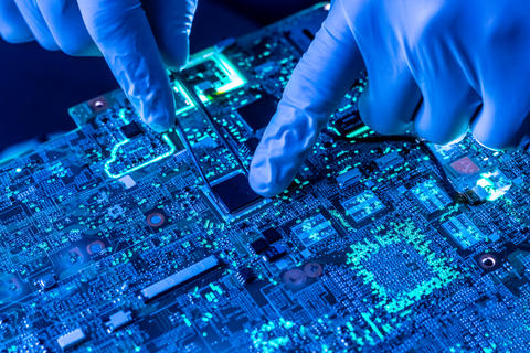 Closeup photo shows person wearing blue gloves using tweezers to work on a semiconductor circuit board.