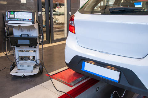 Photograph of an automobile at an emissions testing station, with testing equipment and probe positioned at the car tailpipe.
