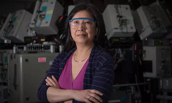 Joannie Chin双手交叉，戴着护目镜，站在科学设备前。 