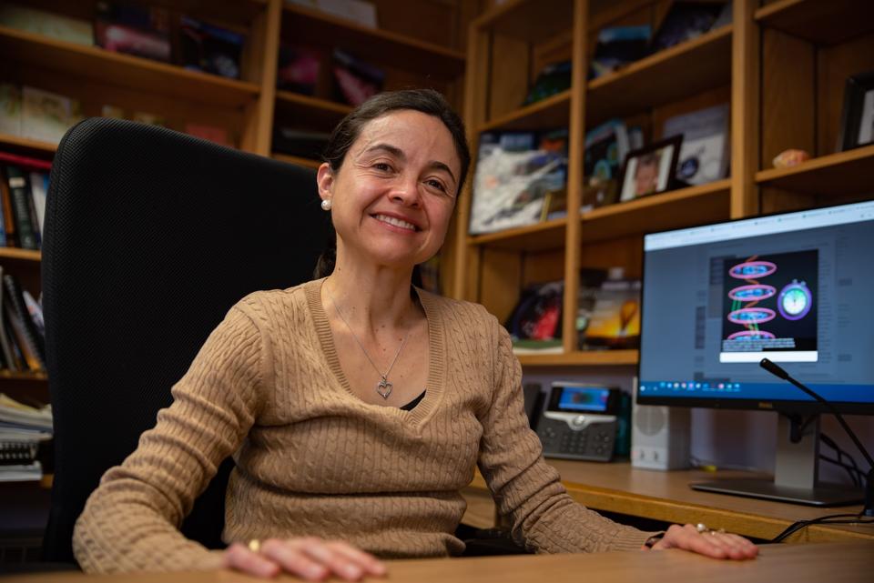 Ana Maria Rey sits at desk in an office and smiles for a photo.