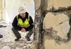 地震后，一名身穿安全装备的男子蹲下检查建筑物内受损的墙壁。 