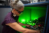 一位戴着安全眼镜的研究人员把手伸进一个装有电路和其他设备的盒子里，盒子发出绿光。 