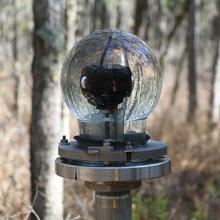 A glass globe on a metal pedestal holds a 360-degree camera in a wooded area.