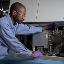 Chemist Savelas Rabb is bent over slightly, using a tool to check on the settings inside of a large instrument known as a mass spectrometer.