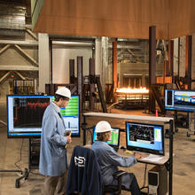 Three individuals watch measurements on a screen while a test fire burns
