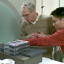 two researchers in front of CT scanner with box of polymer ellipsoids
