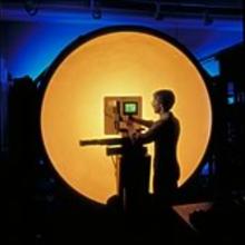 Man with a video display stands in front of a big orange orb of light