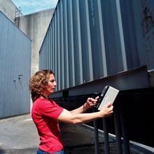 Woman stands holding a radiation detection device in front of a truck
