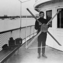Man standing on a boat holding a radio direction finder, which looks like a kite without any fabric