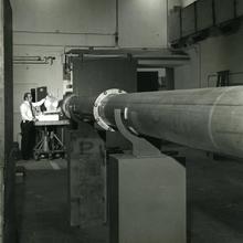 A man stands in the far background at the end of a long metal tube