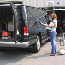 A woman stands next to a van, holding a device against the side of it 