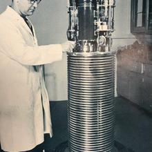 A man in a lab coat stands to the left of a tall piece of equipment