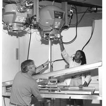 Two scientists on either side of a large machine with overhead components