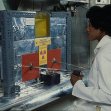 A woman works at a metal machine with a radioactivity warning sticker