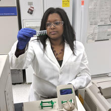 woman in a lab coat looks at vials with a small amount of green liquid in them before putting them into a machine