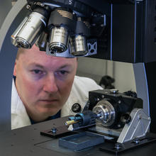 A man looks at the sample held under a microscope.