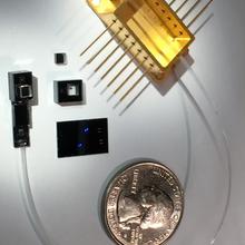 A quarter is shown for scale next to a metal chip and other components.