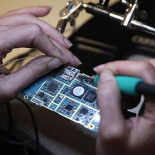 a person's hands as they use a soldering iron to attach wires to a circuit board.