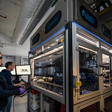 NIST researchers Elizabeth Strychalski and David Ross program the robotic arm that operates within the box-like structure of the NIST biofoundry.