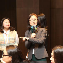 Hae-Jeong Lee speaks into a microphone as a student stands beside her