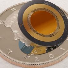 A disk-shaped device is smaller than the half-dollar coin underneath it. 