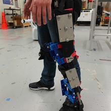 A person wears an exoskeleton and 3D-printed knee apparatus fashioned with reflective markers.