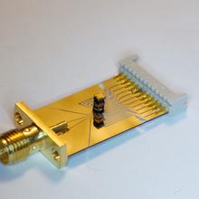 Gold-colored rectangular device with cylindrical attachment on one end. 