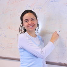 A woman stands at a whiteboard showing scientific formulas.