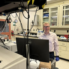 Brad Sutliff wears safety glasses as he stands in the lab in front of a computer monitor.