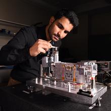 A person in a black shirt works on a mechanical device in a lab setting.