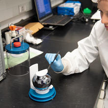 A researcher uses tweezers to adjust a white pad resting on a silvery sphere sitting in a special holder on a lab table. 