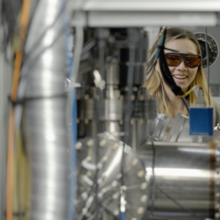 Sun Park, wearing safety glasses, is seen through an opening in an equipment setup in the lab. 