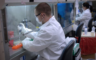 Man in white lab coat using a pipette under a hood