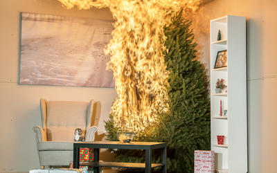 A Christmas tree is engulfed in flames. To the left is a chair. In front is a coffee table, rug and fishbowl. To the right is a tall bookshelf. There are 3 wrapped presents under the tree. A timer reads 8:04 seconds.