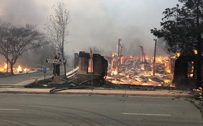 A sign saying "Welcome to Paradise" stands next to a burning building.