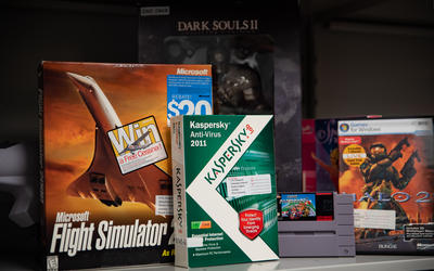 Boxes of old software stand on a shelf, inlcuding a flight simulator, Dark Souls II and a Kaspersky anti-virus product.