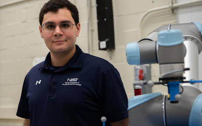 Omar Aboul-Enein poses next to a silver and blue robotic arm in a lab setting.