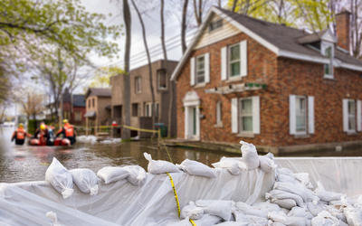 Flood protection sandbags buffer waters around flooded homes with rescue team pushing boat through flooded streets.