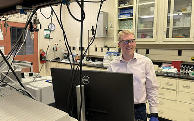 Brad Sutliff wears safety glasses as he stands in the lab in front of a computer monitor.