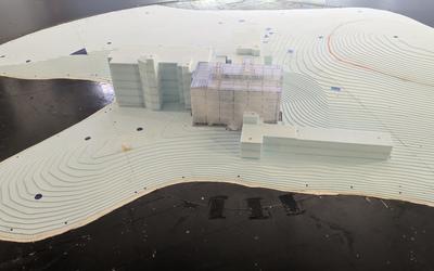 A building model of a hospital site sits on a platform in a long hallway that faces large fans.