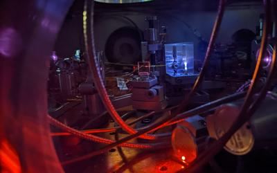 Table in darkened lab holds wiring and other laser electronics; a circular light source is situated above. 