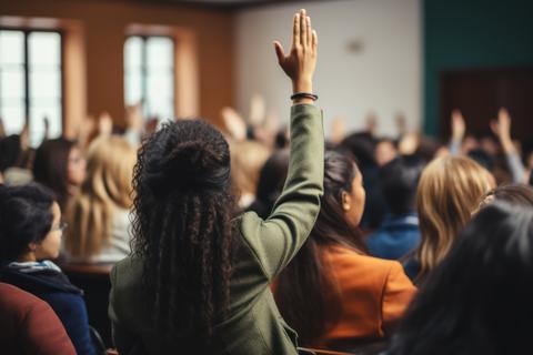 student raising her hand in classroom lecture