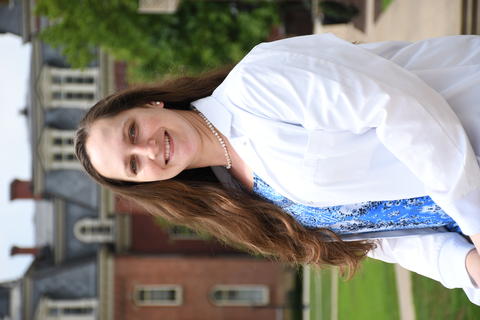 Portrait picture of Korina Menking-Hoggatt,Ph.D, in front of the brick building Wilburn Hall in a lab coat 