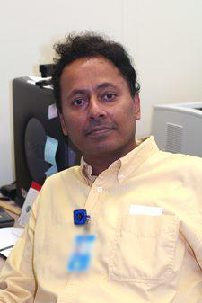 A man with short black hair, wearing a yellow collared button up shirt.